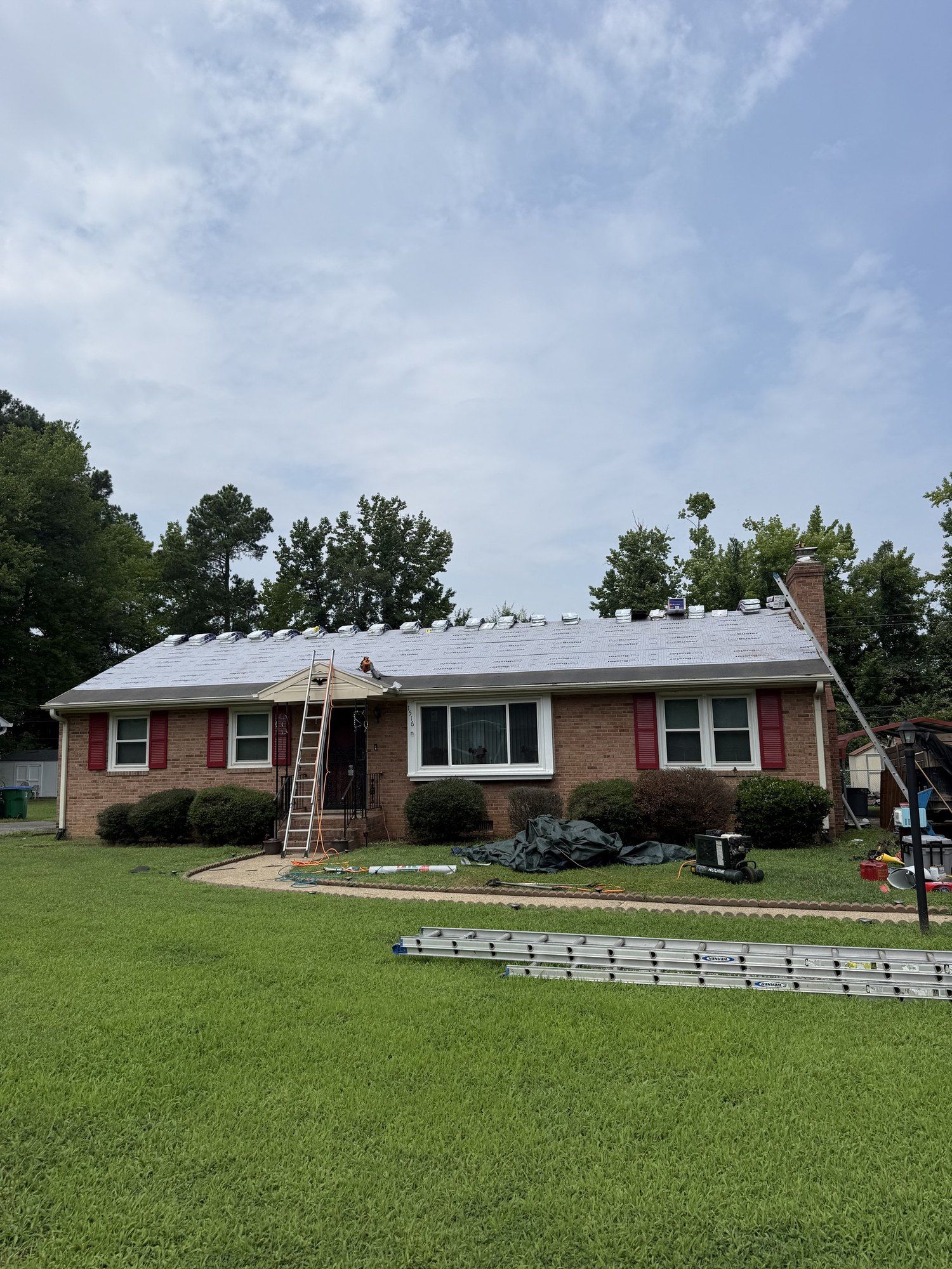 Brick ranch home with red shutters and a new light gray roof, ladder still against the eave