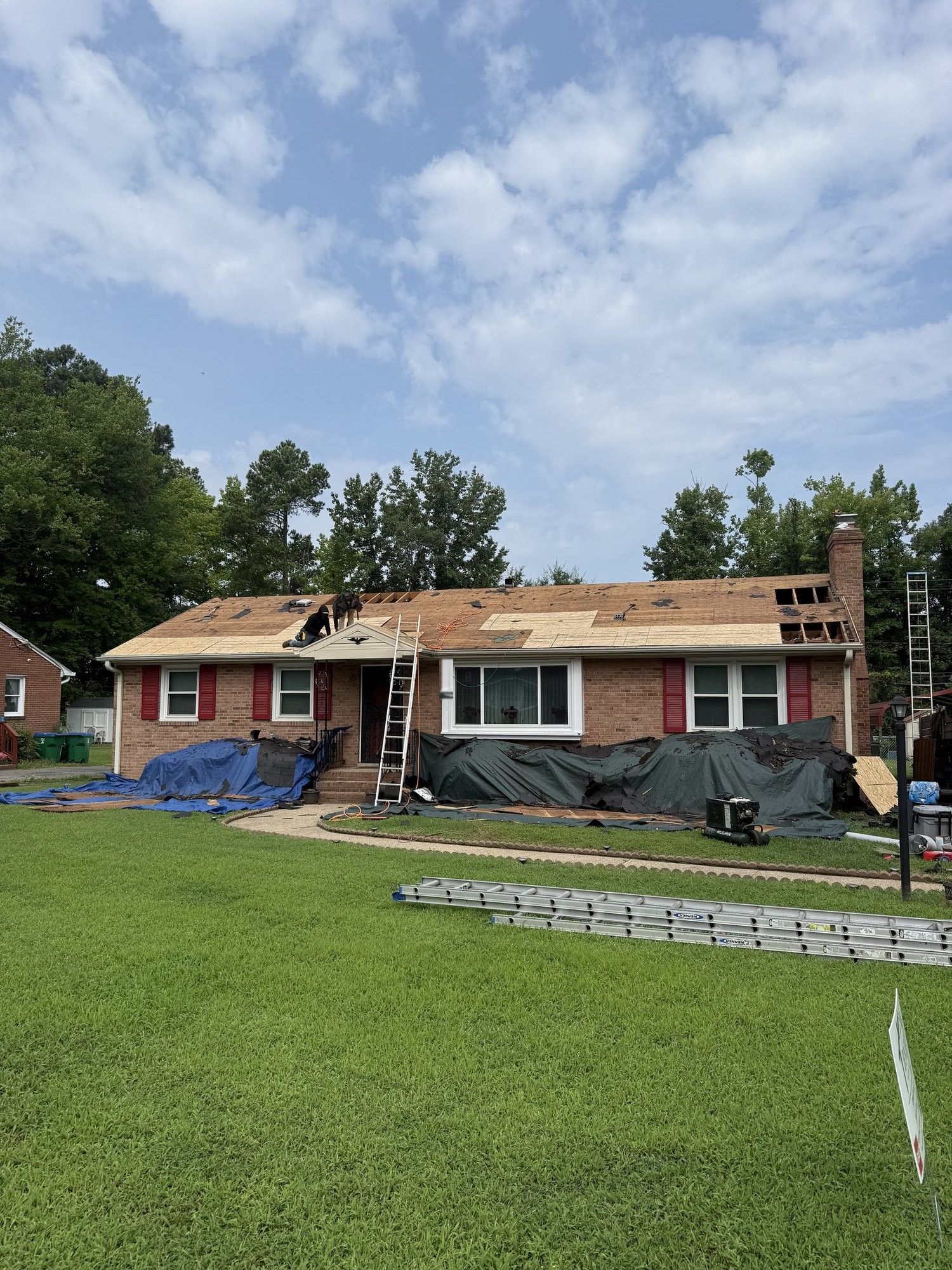 Brick ranch mid tear-off with blue tarps laid over the shrubs and lawn along the front of the house