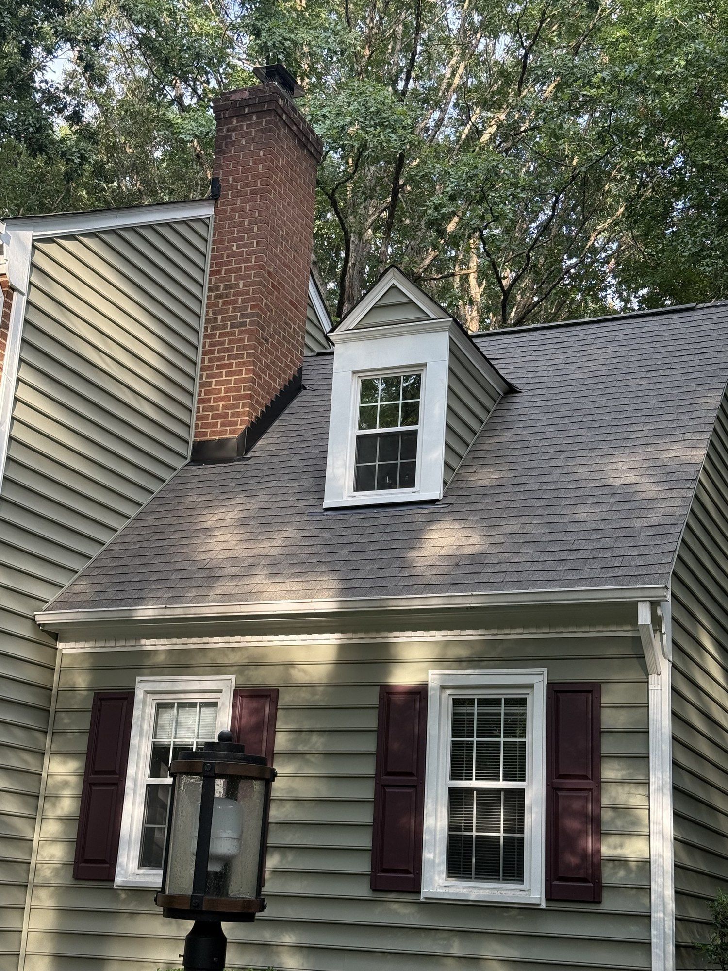 Green-sided Cape with a brick chimney and a single dormer under a new brown-gray shingle roof