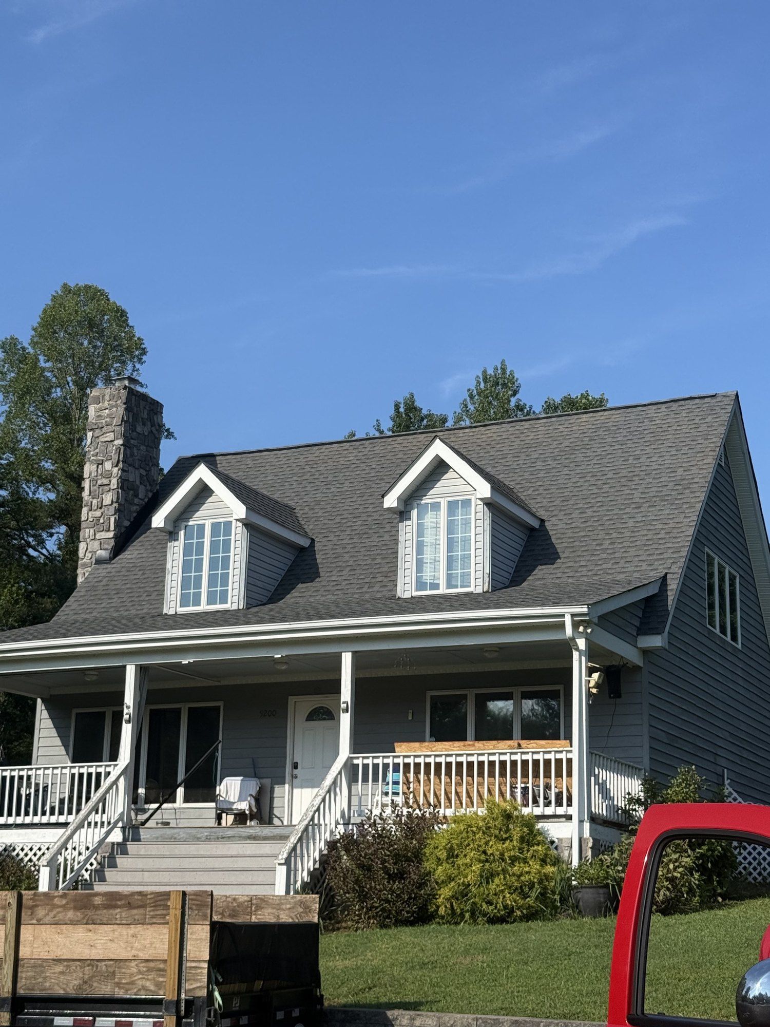 Finished Cape Cod roof with two dormers and a stone chimney, crew trailer in the driveway