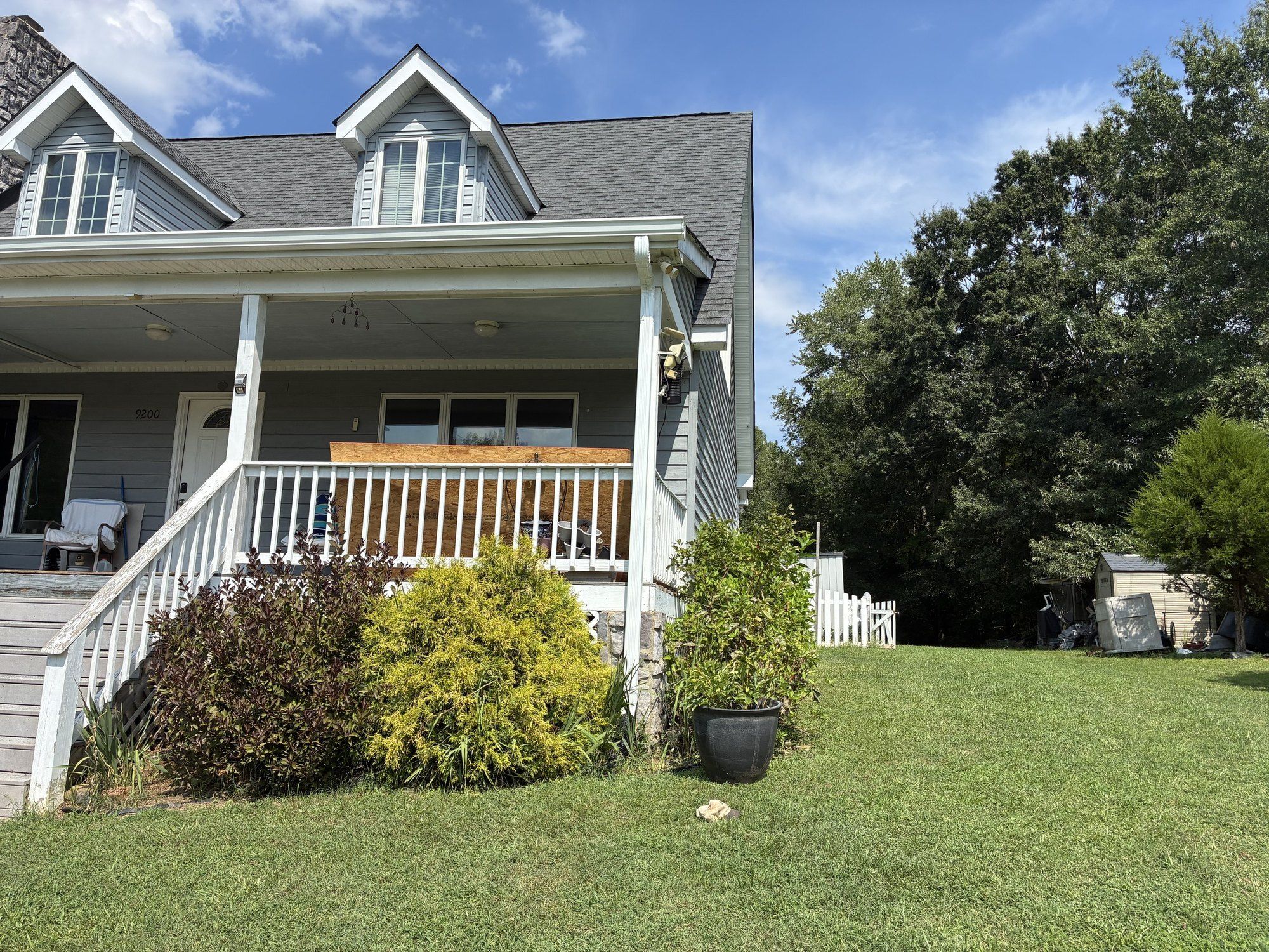 Front porch and dormers of a gray home with a new charcoal shingle roof and white gutters