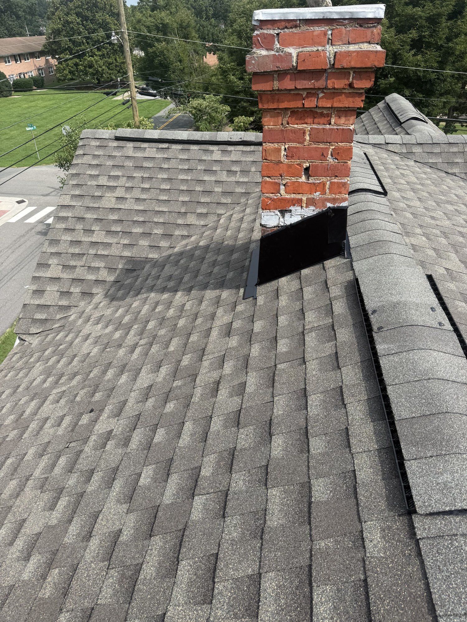 Brick chimney with new metal flashing and fresh gray shingles around its base