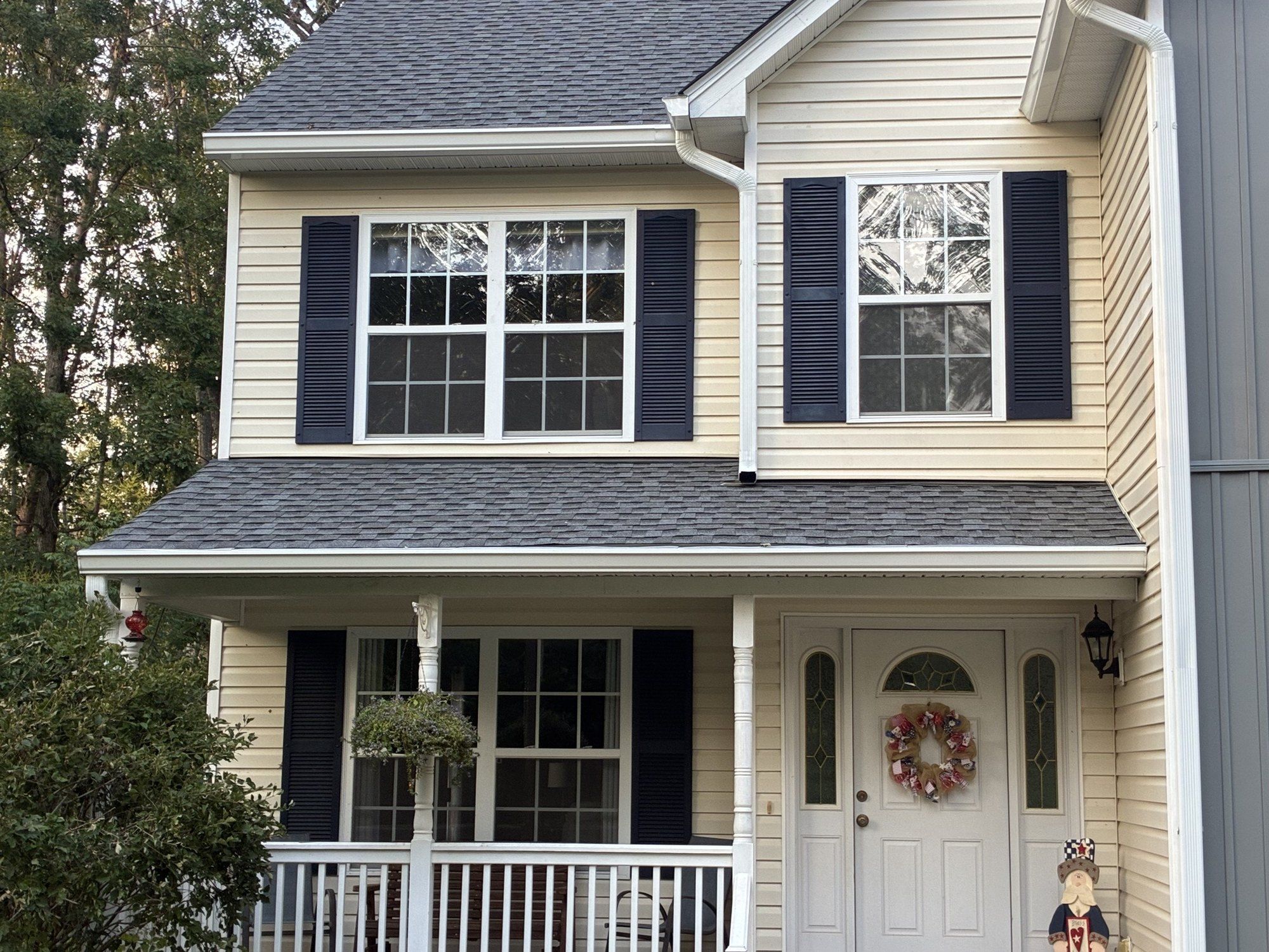 Cream two-story colonial with navy shutters, a new gray porch roof and white gutters and downspouts
