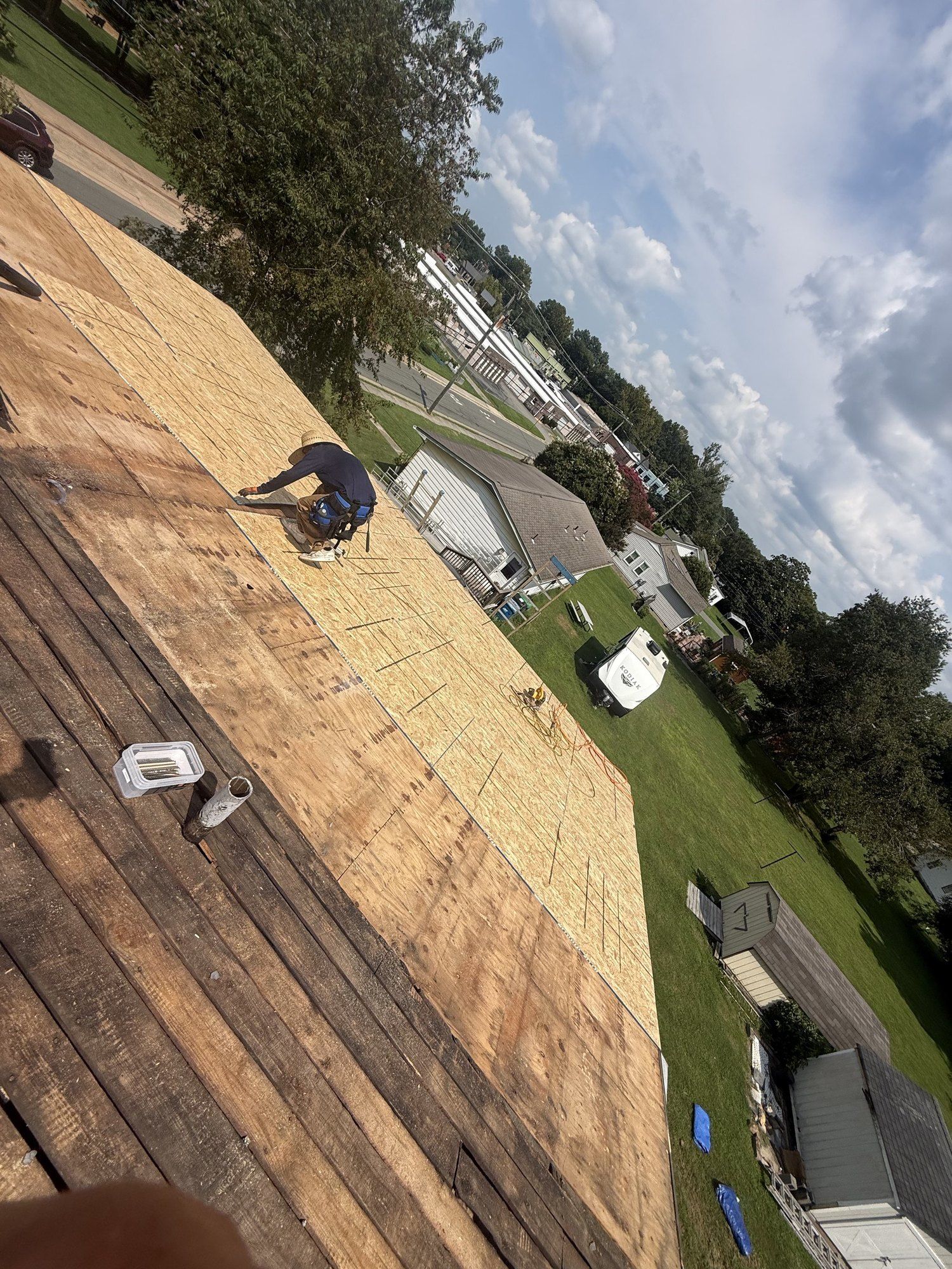 BNH roofer fastening new plywood decking across a roof after tear-off