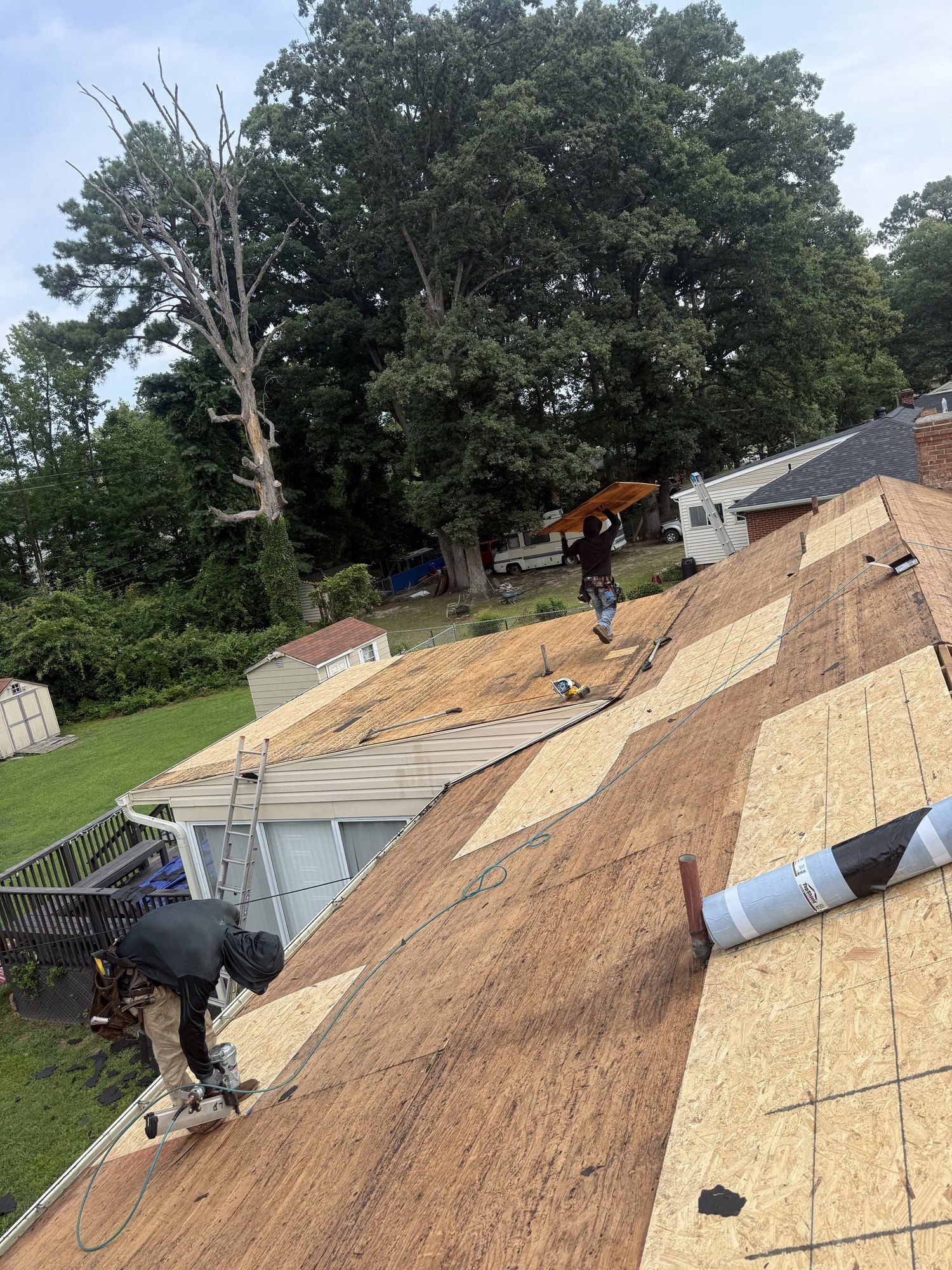 Two BNH roofers working on a roof mid tear-off with new plywood patched into the old deck
