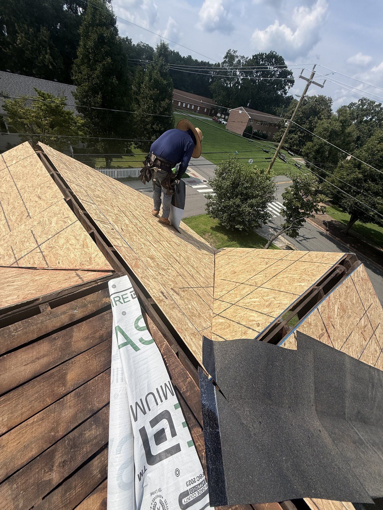 Old plank roof boards beside new plywood sheathing during a re-roof, with a roofer working at the ridge